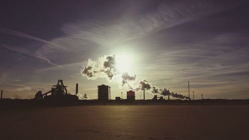 Silhouette of factory against sky