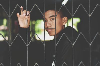 Portrait of young man looking through metal fence