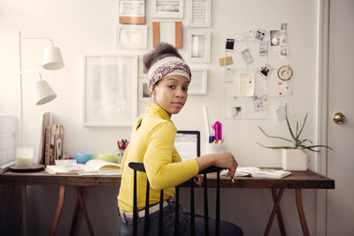 Portrait of woman working on laptop computer at table against papers on wall