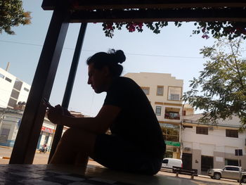 Side view of young man sitting against buildings in city