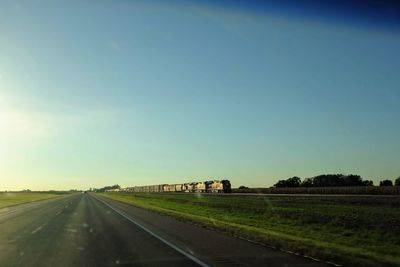 Road amidst field against clear sky