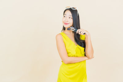Young woman holding yellow while standing against white background