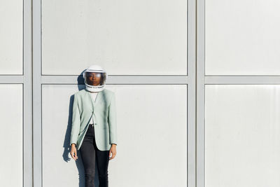 Young businesswoman wearing astronaut helmet in front of wall