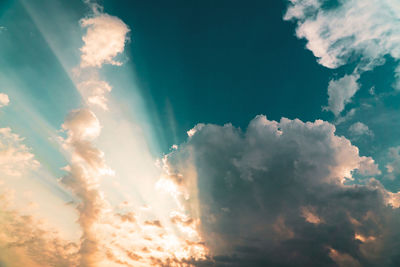 Low angle view of sunlight streaming through clouds