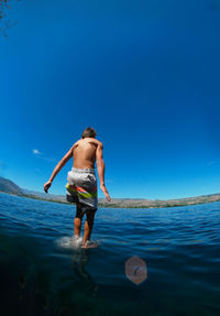 Rear view of boy diving into lake chelan against blue sky
