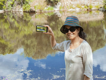 Young woman using mobile phone while standing by water