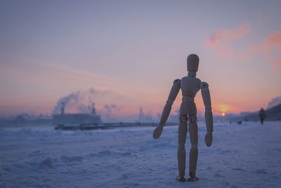 Close-up of wooden figurine on snow covered field against sky at sunset