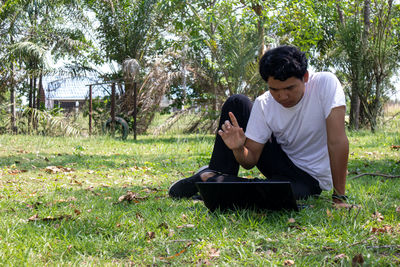 Young man sitting on grass against trees