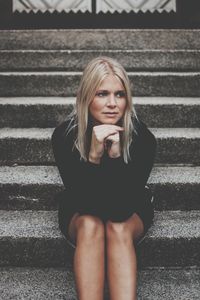 Beautiful young woman with hands on chin looking away while sitting on staircase