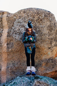 Full length of woman holding camera standing against wall