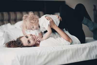 Smiling mother carrying daughter on bed at home