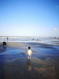 Rear view of baby boy standing at beach against sky