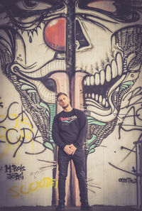 Full length portrait of young man standing against graffiti wall