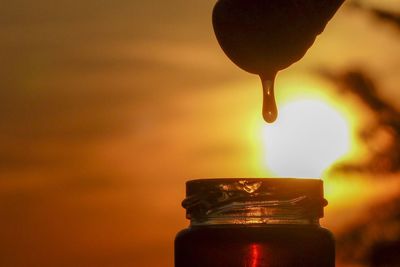 Close-up of glass bottle against orange sunset sky