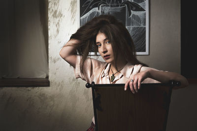 Portrait of woman with hand in hair sitting against wall at home