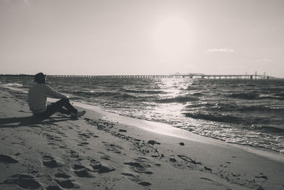 Side view of man looking at sea while sitting against sky