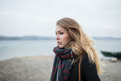 Portrait of beautiful woman standing at beach against sky