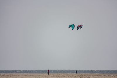 People flying over beach against clear sky