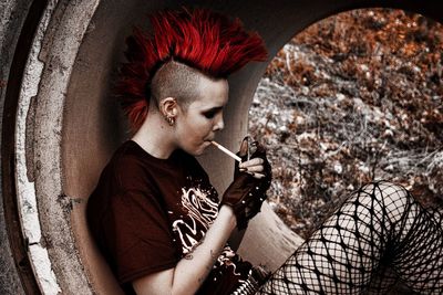 Side view of punk woman smoking cigarette while sitting in pipe