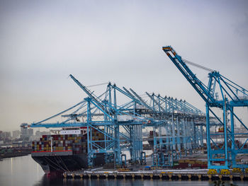 Shipping cranes at dock of harbor port against cloudy sky