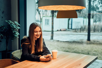 Young woman having a video call, talking remotely, drinking coffee, sitting in a cafe