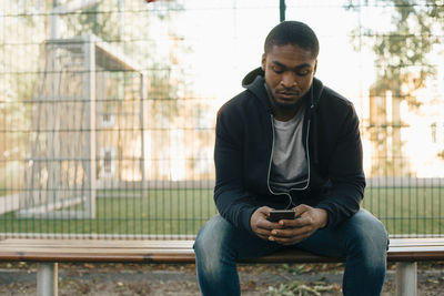 Young man looking away while sitting on mobile phone