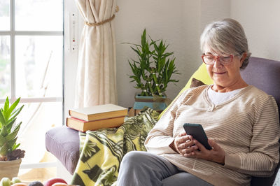 Senior woman using mobile phone while sitting at home