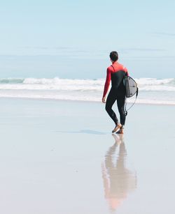 Rear view of man walking on beach against sky