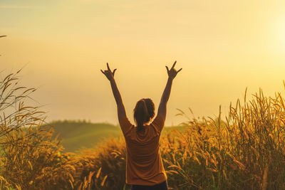 Rear view of woman standing on field against sky during sunset