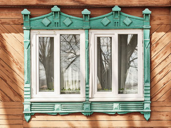 Two windows with shabby carved wooden architraves facade of 19th century wood house, russia.