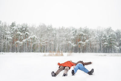 Full length of loving couple lying having fun on snow covered forest