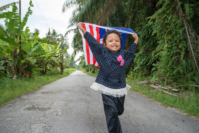 Full length portrait of happy girl on road against trees