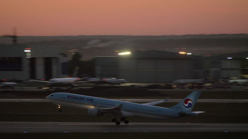 Airplane at airport runway against sky at sunset