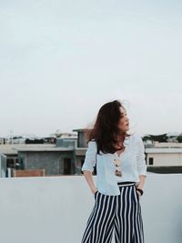 Young woman standing against sky in city