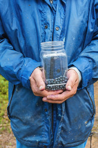 Hand of a picker holding a container with wild blueberries in the forest.