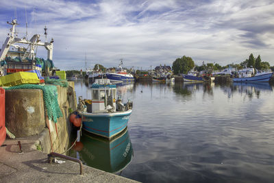 Fishing boats moored at harbor against sky