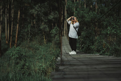 Full length of man photographing while standing on footpath in forest