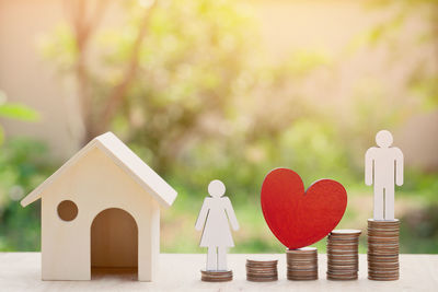 Close-up of model home with figurines and stacked coins on table