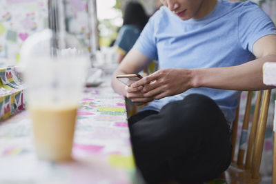 Midsection of woman holding mobile phone while sitting on table