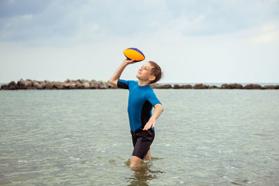 Boy playing with ball in sea against sky
