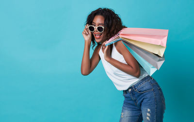 Portrait of happy woman holding shopping bags while standing against turquoise background