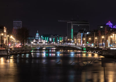 Illuminated bridge over river by buildings against sky at night