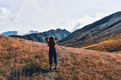 Rear view of woman standing on grass against mountains and sky