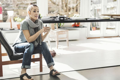 Female architect looking away while sitting on chair in home office