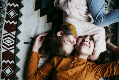 Girl embracing sister face while lying on blanket at home