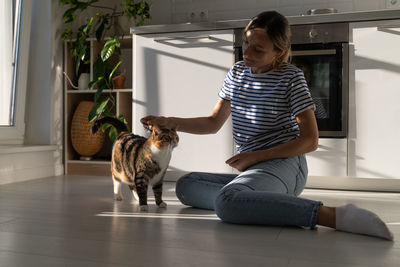 Young woman owner enjoy taking care of beloved cat and combing it sits on floor at home. pet lovers