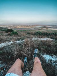 Low section of man relaxing on landscape against sky
