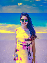 Woman wearing sunglasses standing at beach against sky