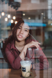 Portrait of smiling woman with drink in restaurant seen through glass