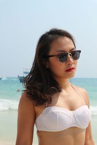 Close-up of young woman wearing sunglasses standing at beach against clear sky